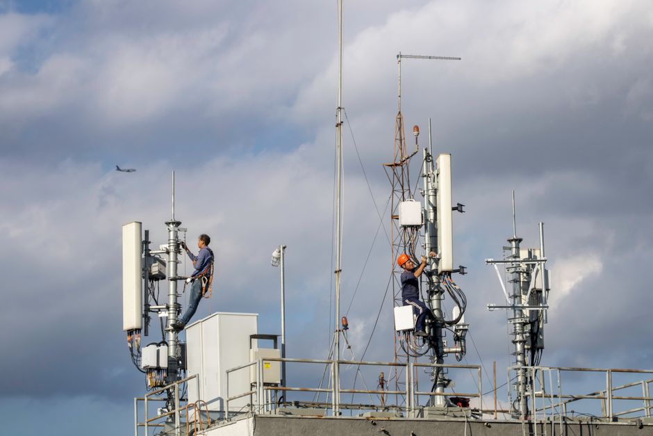 A field technician using instrumentation to check wireless equipment next to an open below-ground water vault.